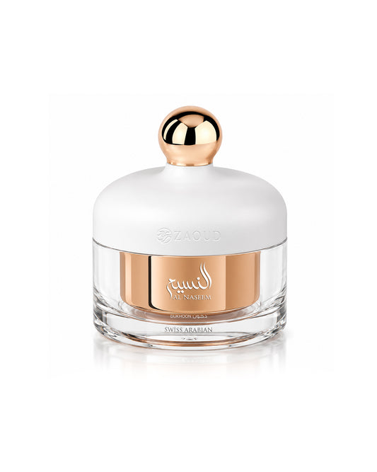 A luxury bakhoor jar from swiss arabian al naseem dukhoon, featuring a white rounded cap with a metallic rose gold spherical knob, a clear glass base, and a central rose gold metallic band with gold Arabic calligraphy.