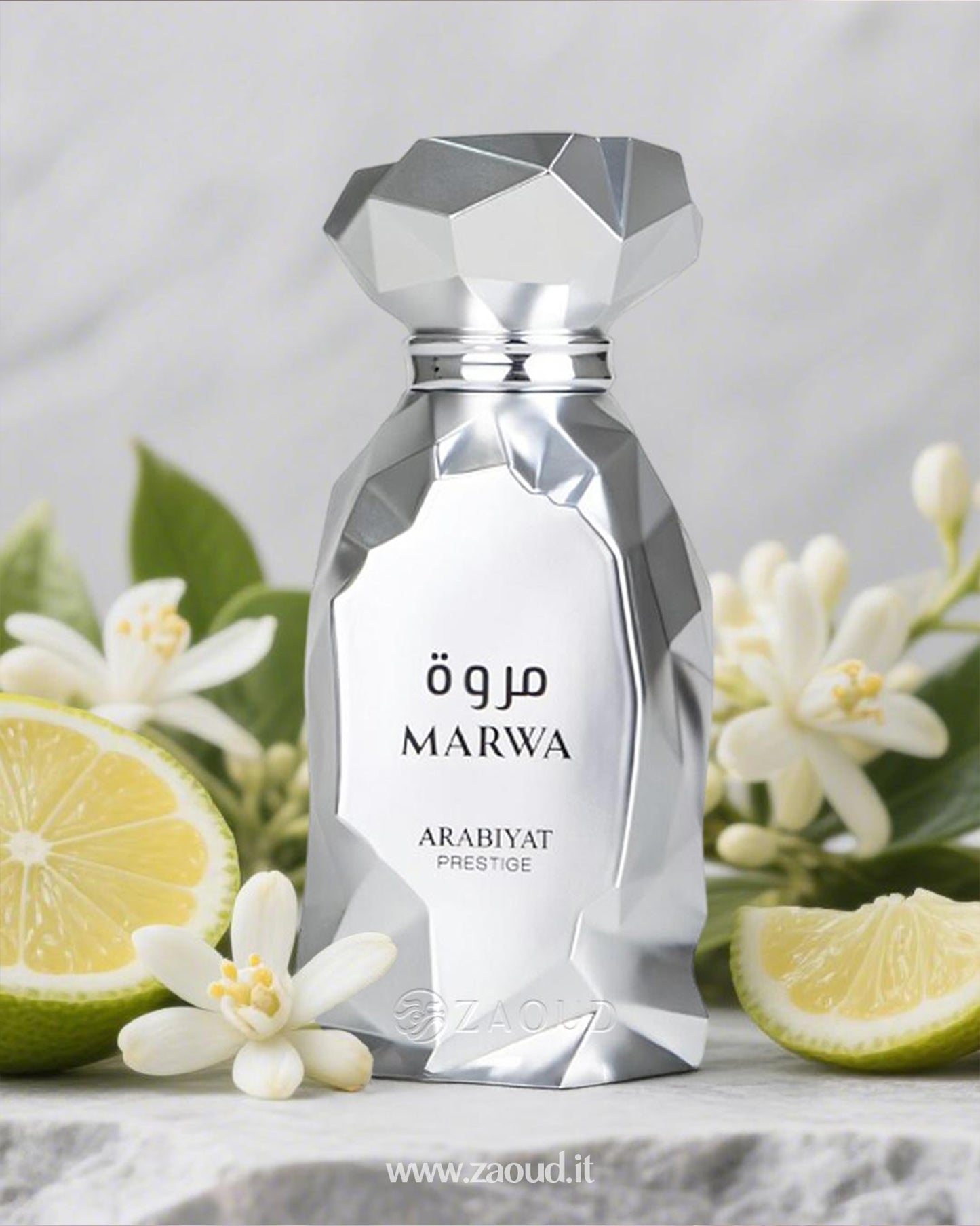 A silver perfume bottle of ‘MARWA’ by ‘ARABIYAT PRESTIGE,’ placed on a marble surface surrounded by white flowers and slices of lime