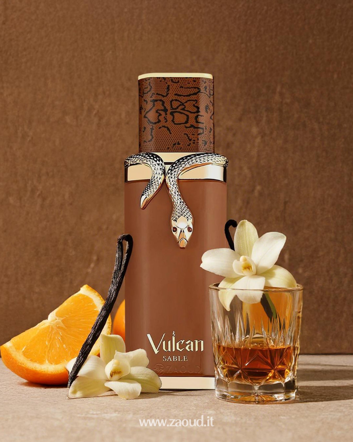 Brown perfume bottle of Vulcan Sable by french avenue, featuring a silver snake design, placed with orange slices, vanilla flowers, vanilla beans, and a glass of whiskey on a warm brown background.