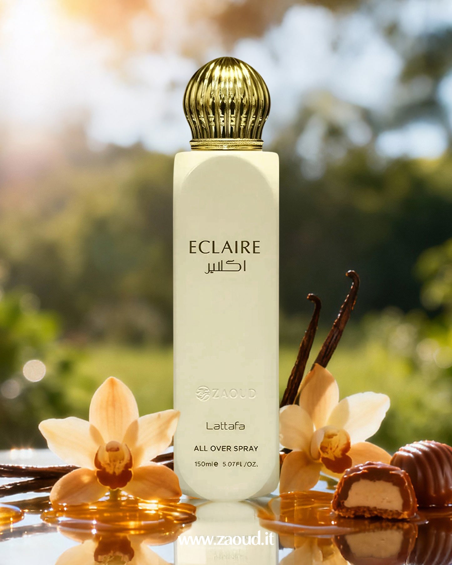 A photo of the Lattafa Eclaire All Over Spray bottle, set on a reflective surface surrounded by vanilla flowers, vanilla pods, honey, and a chocolate praline, with a sunny, blurred green background.