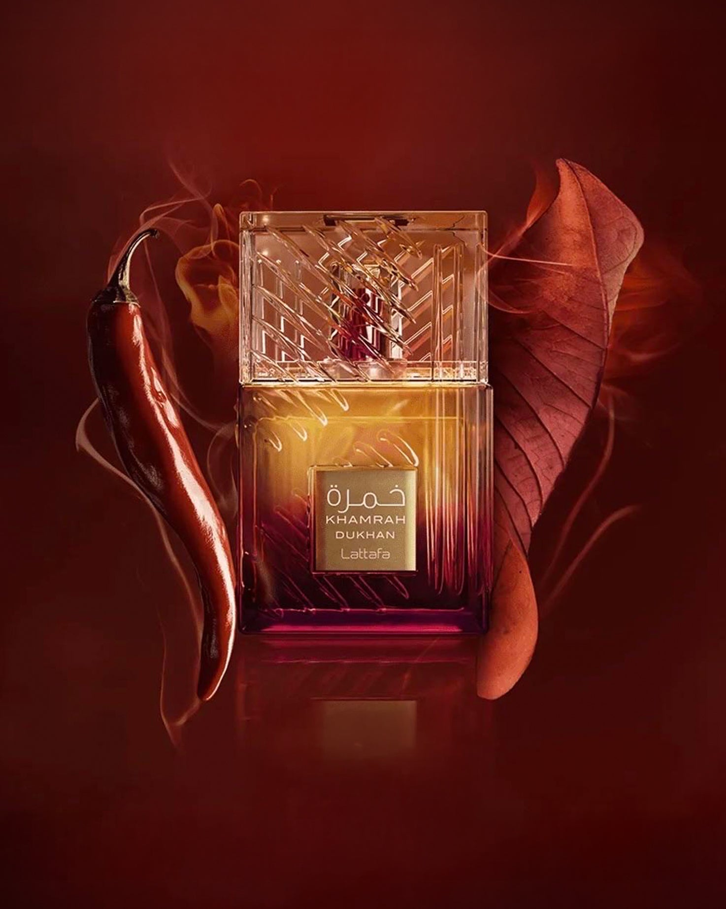 lattafa khamrah dukhan perfume bottle phtograph beside pimento and tobacco leaf against red background