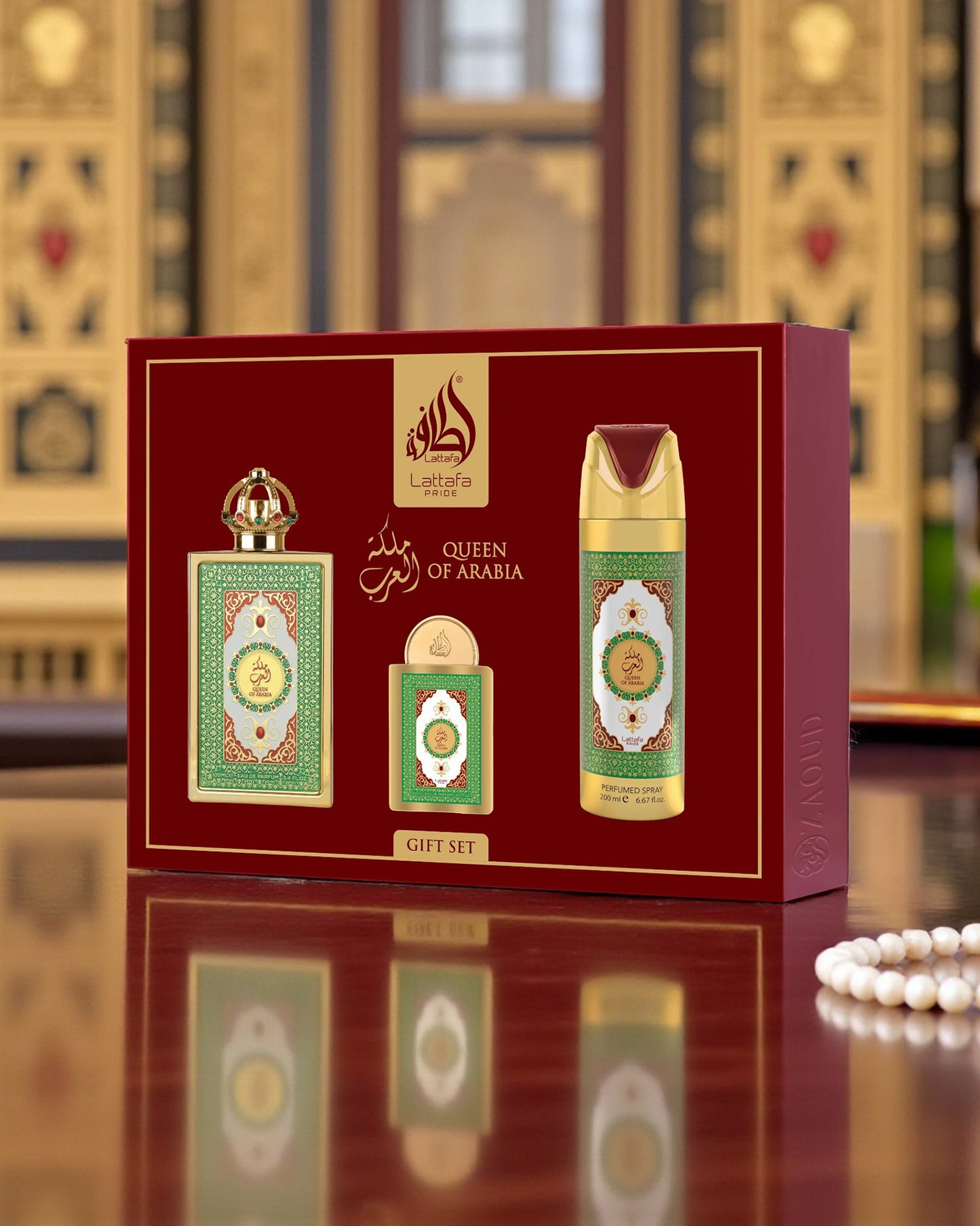 lattafa Queen of Arabia perfume set packaging on a reflective surface with a blurred decorative background.