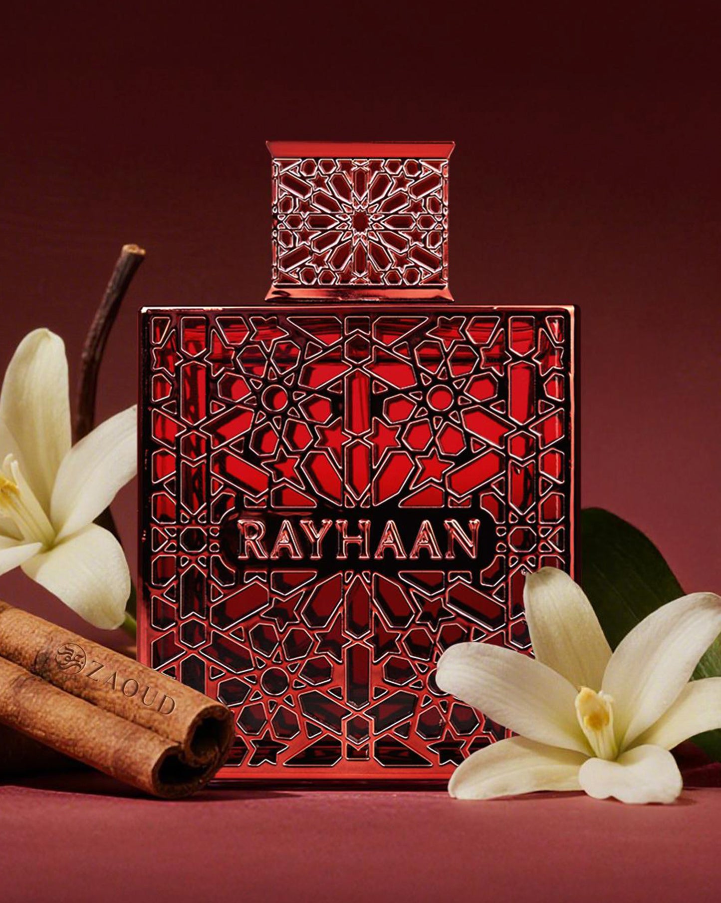 Red perfume bottle of Rayhaan with intricate geometric design, placed with white flowers, cinnamon sticks, and a dark red background.