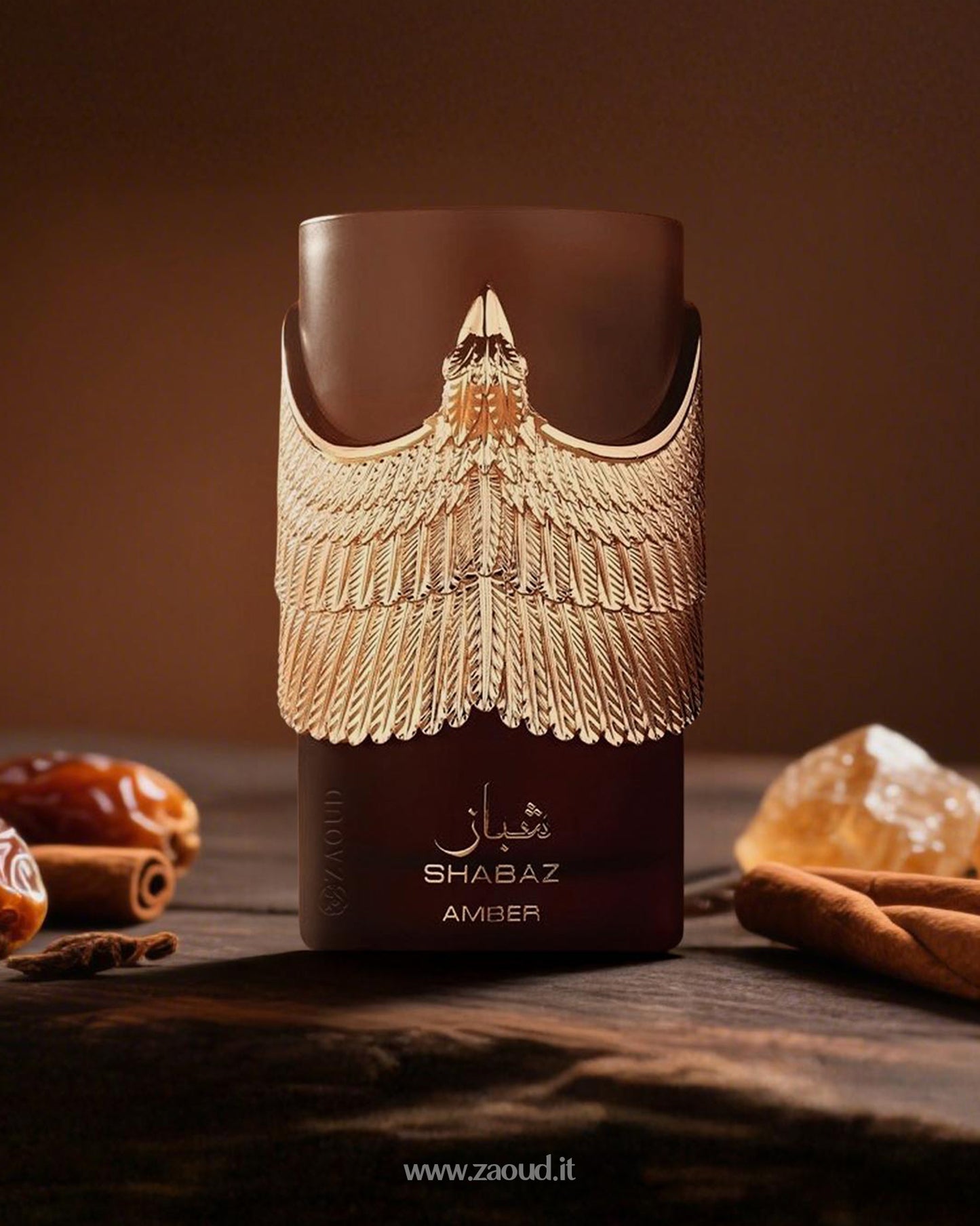 Athoor Al Alam's Shabaz Amber perfume bottle, featuring a luxurious gold winged design on a deep brown bottle, surrounded by cinnamon sticks, dates, and amber crystals, set against a rich brown background.