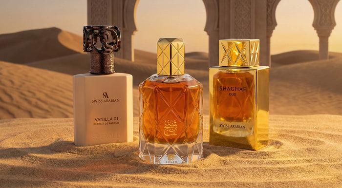 Luxury Arabic perfumes displayed in desert setting – Swiss Arabian Vanilla 01, Ahmed fragrance bottle, and Shaghaf Oud by Swiss Arabian with golden Arabian architecture background.