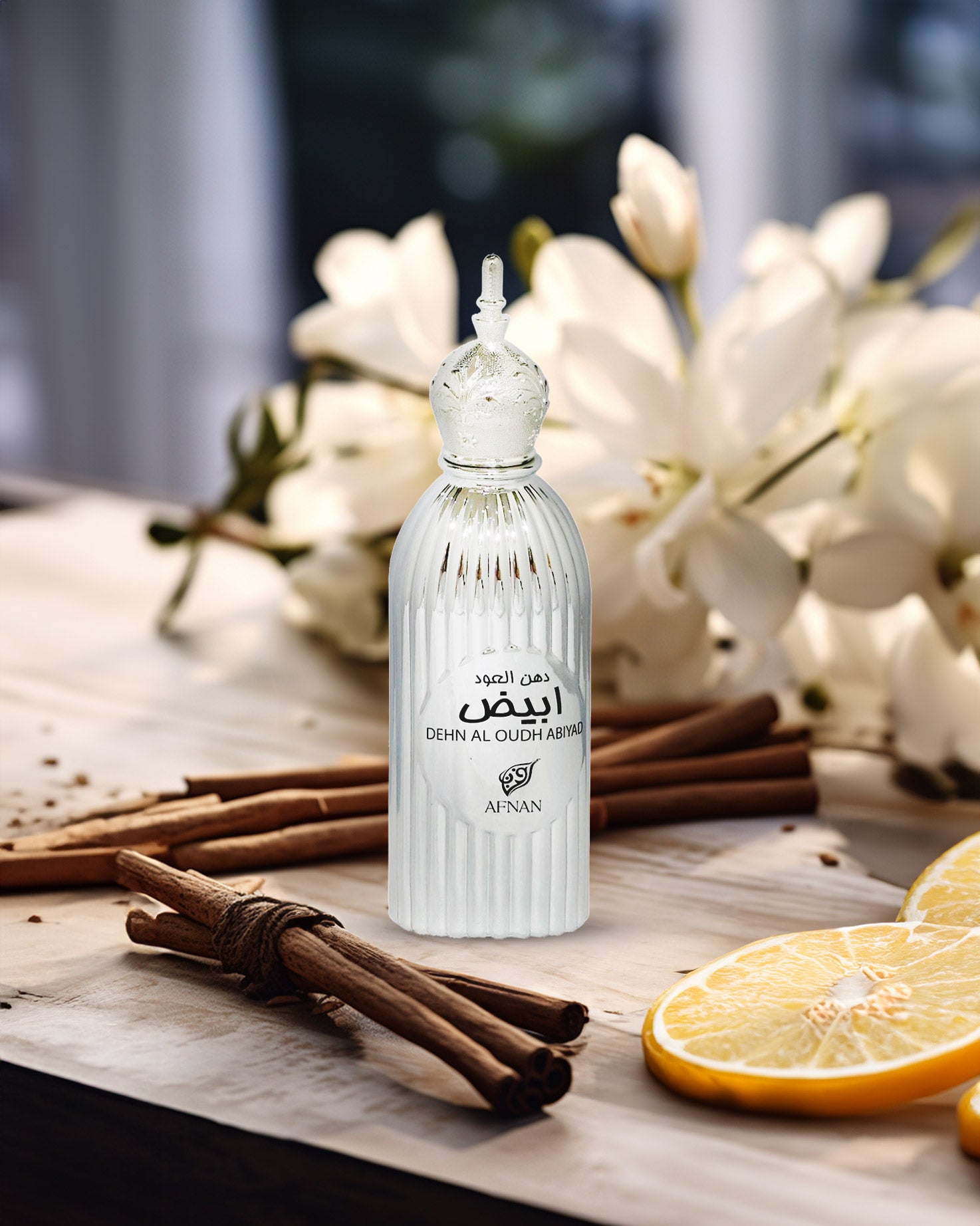 Afnan Dehn Al Oudh Abiyad perfume bottle photograph besides citrus cinnamon behind white flowers