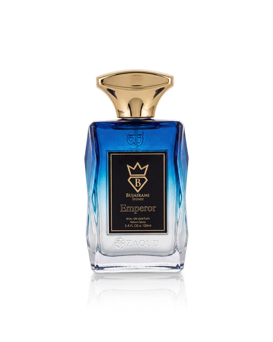 A faceted glass bottle of bujairami Emperor perfume, featuring a vibrant blue gradient body, a polished gold cap, and a black label with gold lettering, set against a clean white background with a subtle reflection.