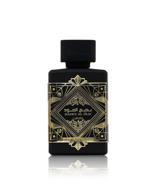 lattafa badee al oud oud for glory perfume bottle with a black cap, featuring an ornate gold geometric label with Arabic and English text, set against a clean white background with a soft reflection below.