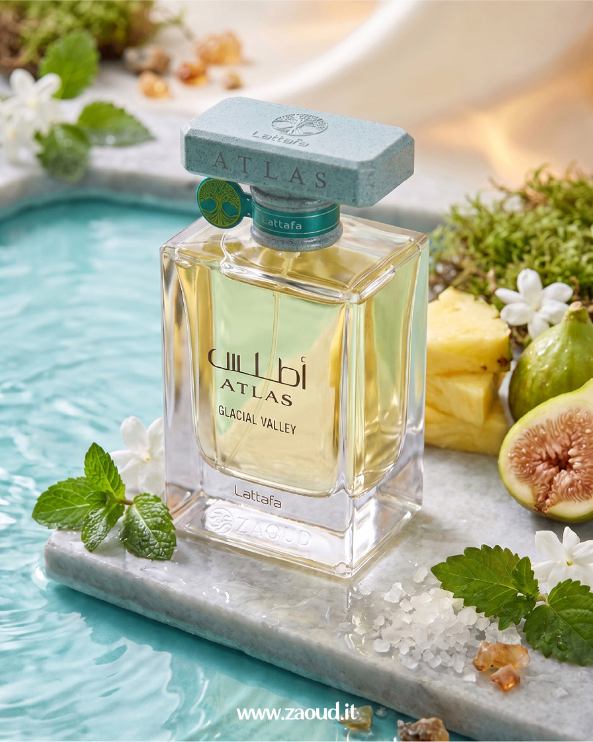 A bottle of Lattafa Atlas Glacial Valley perfume is displayed on a marble slab in a turquoise pool, surrounded by mint leaves, white flowers, a pineapple slice, and a fig.