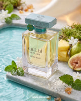 A bottle of Lattafa Atlas Glacial Valley perfume is displayed on a marble slab in a turquoise pool, surrounded by mint leaves, white flowers, a pineapple slice, and a fig.