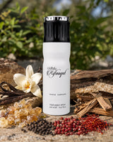 A white perfume spray bottle with a black cap stands on a stone surface outdoors, surrounded by dried botanicals, spices, and a white flower. The bottle is branded 'Oldaj Rifaqar' and reads 'Paris Corner Perfumed Spray 230 ml'.