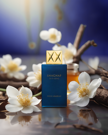 Swiss Arabian Shaghaf Oud Azaq perfume bottle with golden logo surrounded by white blossoms and vanilla pods on a reflective surface with a blurred blue background.