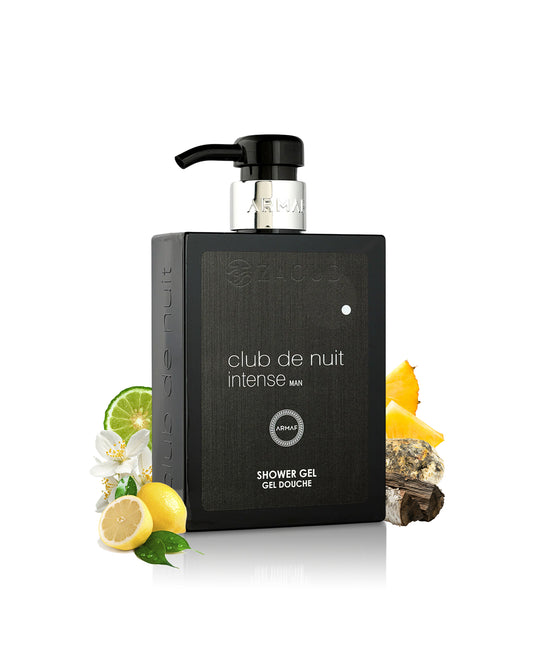 A black rectangular shower gel bottle with a black pump dispenser, labeled 'club de nuit intense MAN', styled with citrus fruits, a lime slice, white flowers, and bark on a white background.
