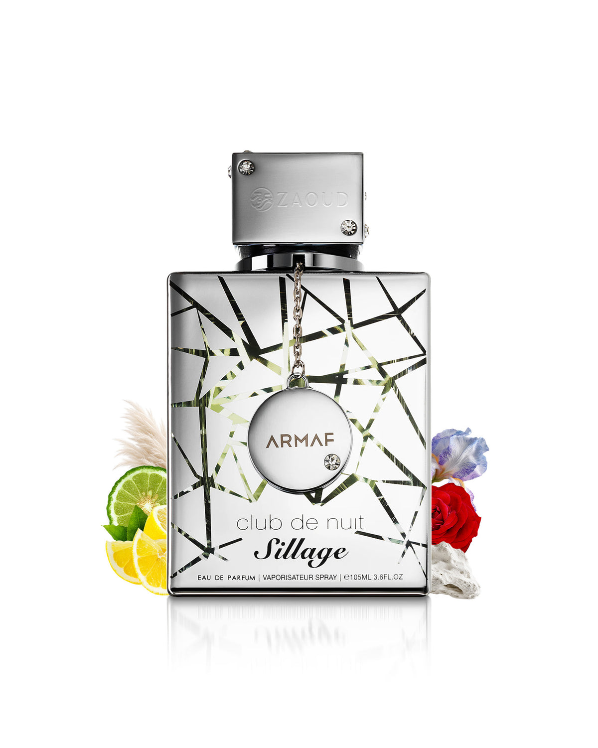 Armaf Club de Nuit sillage Eau de Parfum bottle with a silver cap and a geometric black and green patterned glass body, styled with citrus slices, flowers, and pampas grass on a white background.