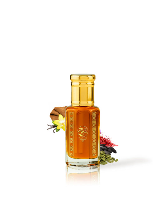 karam perfume oil bottle filled with amber-orange liquid, topped with a shiny gold cap, and decorated with dried botanicals including a vanilla pod, vanilla flower, and red and green seeds, set against a solid white background.