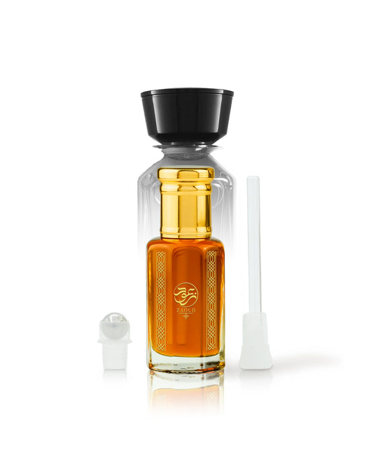 karam perfume oil bottle filled with amber-orange liquid, topped with a black cap, shown on a white background with a small white spray atomizer and a white applicator tube beside it.