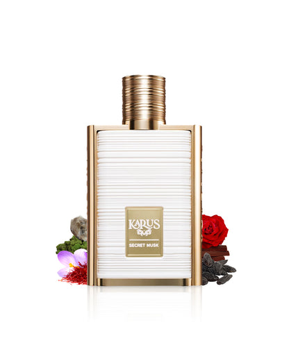 karus secret musk by khadlaj perfume bottle surrounded with its ingredients like rose and saffron shows from behind the bottle against white background