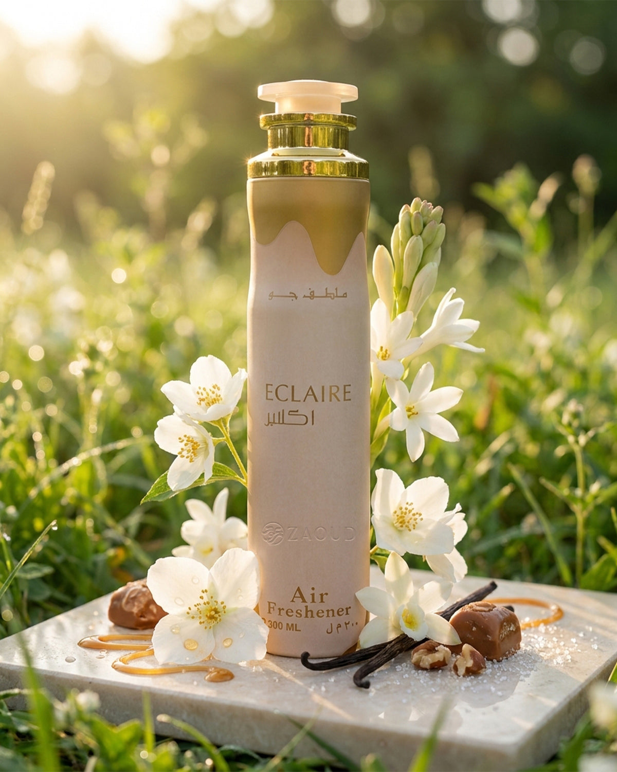 lattafa Eclaire Air freshener is styled outdoors on a stone slab with white flowers, vanilla beans, and nuts, set against a blurred green grassy background with warm sunlight.