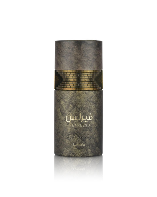 A cylindrical perfume bottle from the brand lattafa, named Fearless, featuring a textured dark gray and gold marble-like design with a gold brick pattern band around the middle and gold Arabic lettering.