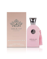 A pink Delilah pour femme Parfum bottle with a silver cap and a pink tassel, displayed next to its matching pink packaging box on a reflective white surface.