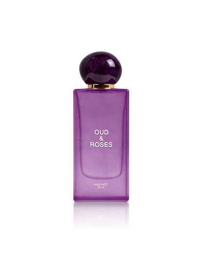 A purple rectangular bottle of Oud & Roses Hair Mist 100ml with a spherical dark purple cap and gold collar, centered on a white background with a soft reflection.