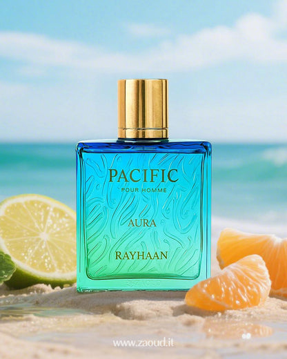 Blue and green gradient perfume bottle of Pacific Aura by Rayhaan placed on sandy beach, surrounded by mint leaves, lime, and orange slices, with ocean waves and palm trees in the background.