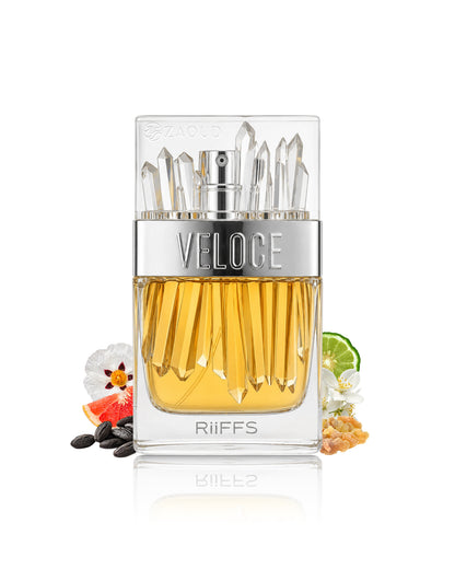 A clear rectangular perfume bottle filled with golden amber liquid, with a silver band reading VELOCE and clear faceted crystal-like tops. The bottle is centered on a white background with small decorative botanical and spice accents around the base.