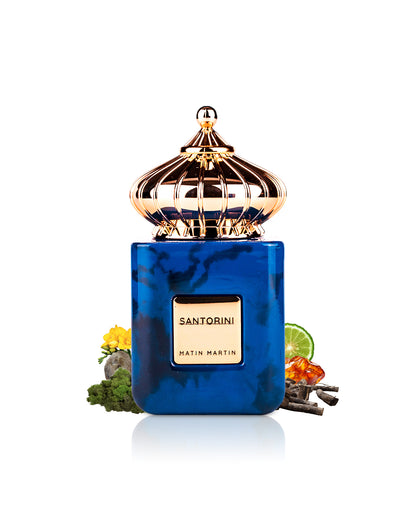 matin martin santorini perfume bottle surrounded with fragrance notes like amber and woods shows from behind the bottle against white background