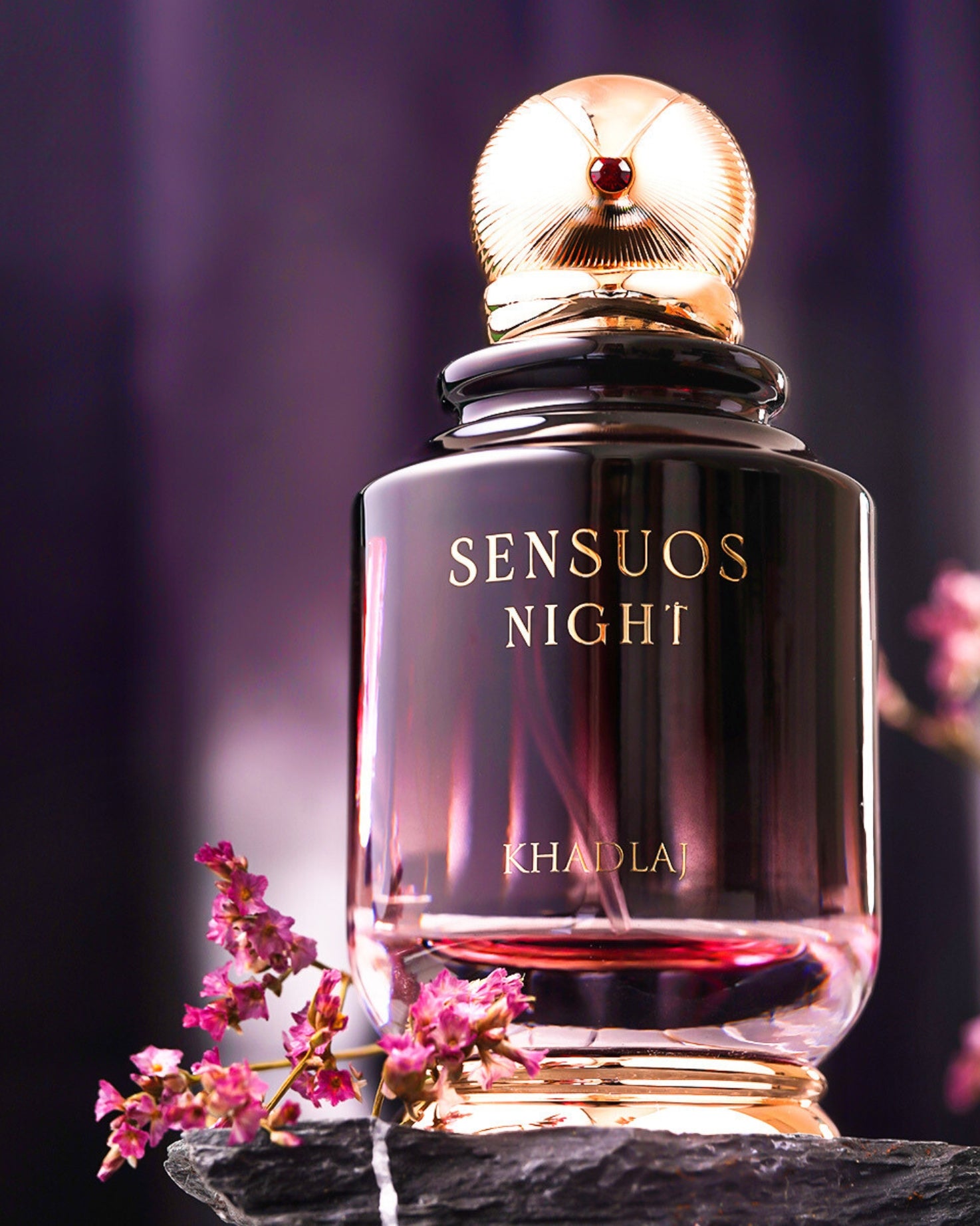 sensuos night edp by khadlaj perfume bottle  photograph over a rock piece with beside red flowers against blurry background