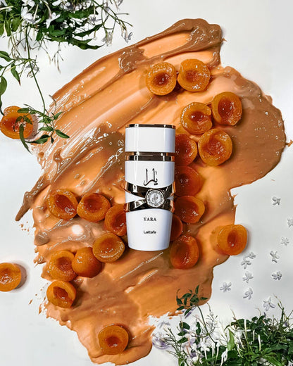 yara moi by lattafa perfumes bottle photograph over creamy caramel and half cut peaches beside some white flowers