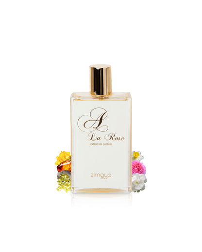 zimaya a la rose extrait de arfum bottle surrounded with its ingredients like rose and osmanthus shows fro behind the bottle  against white background